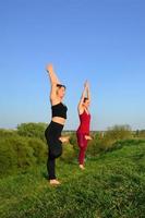 två ung ljushårig flickor i sporter kostymer öva yoga på en pittoresk grön kulle i de öppen luft i de kväll. de begrepp av sport utövar och friska livsstilar foto