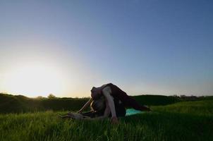 två ung ljushårig flickor i sporter kostymer öva yoga på en pittoresk grön kulle i de öppen luft i de kväll. de begrepp av sport utövar utomhus foto