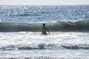 bak- se av bar överkropp man gående mitt i hav på san Diego foto