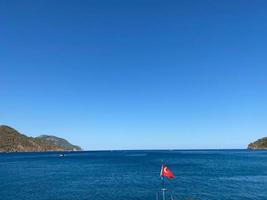 de vinka turkiska flagga på en lugna hav bakgrund med en båt och blå himmel foto