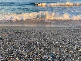 vågor av vatten i de hav och sand med små naturlig flerfärgad stenar på de stranden, små småsten på de strand. bakgrund, textur foto