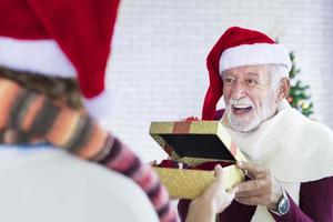 senior caucasian farfar ger jul närvarande till de familj medlem för fira jul tillsammans i lycka och spänning på Hem med santa hatt foto
