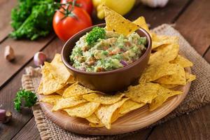 guacamole avokado, lime, tomat, lök och koriander, serveras med nachos - traditionellt mexikanskt mellanmål foto