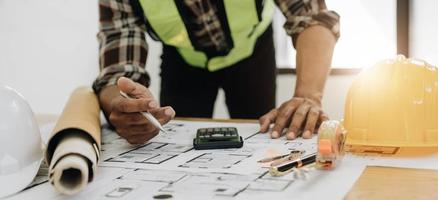 stänga upp av civil manlig ingenjör asiatisk arbetssätt på plan arkitektonisk projekt på konstruktion webbplats på skrivbord i kontor. foto