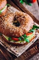 bagels med grädde, avokado, tomater och arugula på trä- styrelse. friska frukost mat. foto