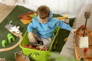 liten caucasian pojke med blå luvtröja spelar med färgrik leksaker på Hem. barn har roligt. Lycklig och glad unge spelar med fartyg, dinosaurier, slott. fritid aktivitet, inhemsk liv. selektiv fokus foto