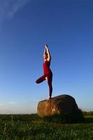 silhuett av ung blond flicka i sport kostym öva yoga på en pittoresk grön kulle i de kväll på solnedgång. de begrepp av utövar och friska livsstilar foto