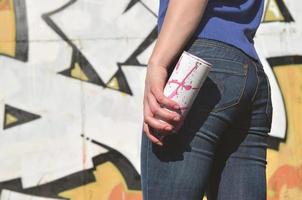 Foto av en flickans hand med aerosol måla burkar i händer på en graffiti vägg bakgrund. de begrepp av gata konst och använda sig av av aerosol färger. graffiti konst affär bakgrund bild