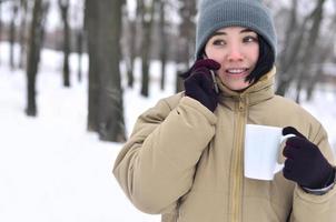 vinter- porträtt av ung flicka med smartphone och kaffe kopp foto