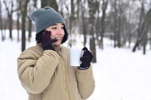 vinter- porträtt av ung flicka med smartphone och kaffe kopp foto