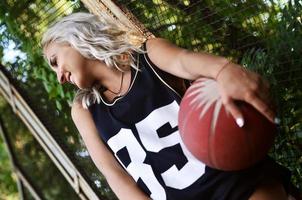 ung blond flicka med orange basketboll Framställ utomhus foto