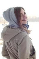 en ung och leende caucasian flicka utseende runt om de horisont linje mellan de himmel och de frysta sjö i vinter- tid foto