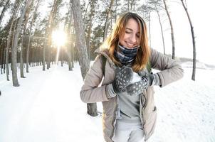 en ung och glad caucasian flicka i en brun täcka skulpterar en snöboll i en snötäckt skog i vinter. spel med snö i de öppen luft. fisköga Foto