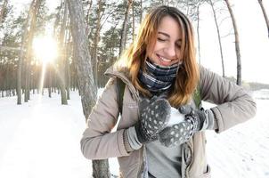 en ung och glad caucasian flicka i en brun täcka skulpterar en snöboll i en snötäckt skog i vinter. spel med snö i de öppen luft. fisköga Foto