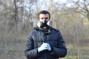 suddig porträtt av ung man i skyddande gas mask bär sudd disponibel handskar utomhus i vår trä foto