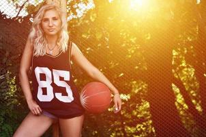 ung blond flicka med orange basketboll Framställ utomhus foto
