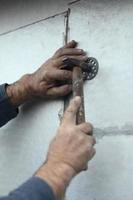 ett äldre workman träskor en tapp in i en plast paraply montera i en Frigolit vägg. de bearbeta av fixering expanderat polystyren tallrikar. uppvärmningen av de Fasad av de byggnad foto
