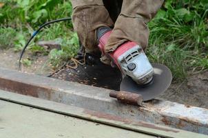 elektrisk hjul slipning på stål strukturera utomhus. gammal manuell arbetstagare i skyddande handskar skärande metall dörr med kvarn foto