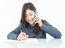 kvinna använder sig av mobil telefon och skrivning anteckningsbok foto