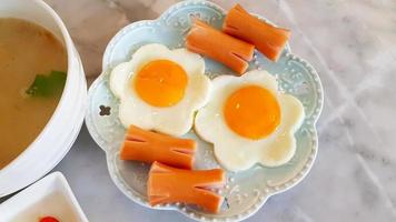 morgon- frukost med blomformad friterad ägg och skivad korv på maträtt eller tallrik med kokt ris i thai stil på marmor tabell och kopia Plats. stänga upp mat foto