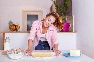 kök förbereder mjöl degglad attraktiv ung vuxen kvinna lady hemmafru bagare innehav stift rullande deg på kök tabell bakning bakverk begrepp matlagning kaka kex håller på med bageri på Hem foto