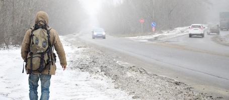 en man med en stor ryggsäck promenader längs en förorts asfalt väg foto