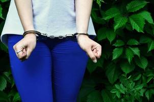 fragment av en ung kriminell flickans kropp med händer i handklovar mot en grön blomstrande murgröna löv bakgrund. de begrepp av frihetsberövande ett lagbrytare av en kvinna kriminell i en lantlig miljö foto