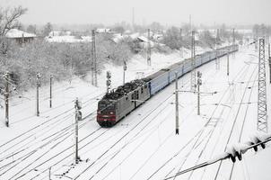 en lång tåg av passagerare bilar är rör på sig längs de järnväg Spår. järnväg landskap i vinter- efter snöfall foto