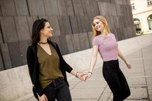 två ung kvinnor gående på de gata och innehav händer foto