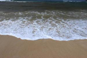 hav Strand med sandig strand och framåt Vinka. vatten skum med slät sand. skön vågor på de sand strand bakgrund. foto