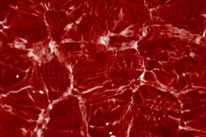 defokusering suddig transparent röd färgad klar lugna vatten yta textur med stänk och bubblor. trendig abstrakt natur bakgrund. vatten vågor i solljus med kopia Plats. röd vattenfärg lysande foto