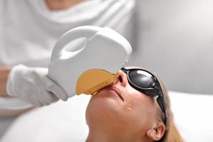 kosmetolog ger epilering laser behandling till kvinna på ansikte foto
