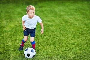 liten pojke praktiserande fotboll utomhus foto
