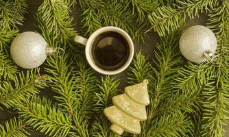 jul kaffe. en kopp av kaffe, två jul silver- bollar och gyllene gran träd leksak på gran träd bakgrund, topp se. foto
