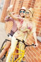 två flicka vänner ridning tandem cykel foto