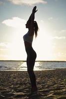 silhuett ung kvinna öva yoga på stranden vid solnedgången foto