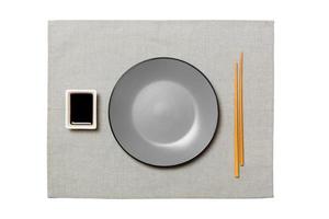 tömma runda grå tallrik med ätpinnar för sushi och soja sås på grå servett bakgrund. topp se med kopia Plats för du design foto