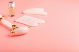 gua sha massage verktyg tillverkad av naturlig rosa kvartsvals, jade sten och olja, på en rosa bakgrund för ansikte och kropp vård. del av traditionell kinesisk medicin foto