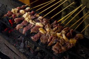 sate kambing eller satay get, lamm, lamm eller kött get satay med träkol ingrediens på röd brand grillning förbi människor. traditionell satay från yogyakarta, java, indonesien matlagning satay foto