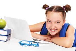 Lycklig flicka håller på med läxa på dator foto