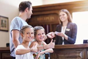 Lycklig familj kontroll i hotell på reception skrivbord foto