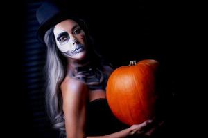 läskigt porträtt av kvinna i halloween gotisk smink innehav pumpa foto
