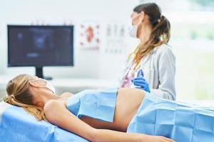 läkare i mask håller på med ultraljud till henne gravid patient foto