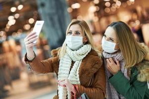 porträtt av två vänner handla tillsammans använder sig av smartphone och bär en mask foto