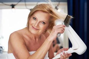 senior kvinna torkning hår i de badrum foto