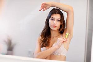 ung kvinna rakning armhålor i badrum i de morgon- foto