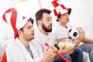 Lycklig manlig vänner glädjande och tittar på sporter på TV foto