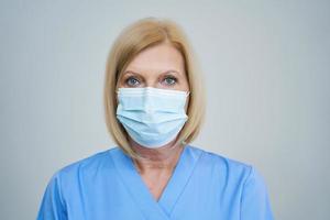 senior kvinna läkare Framställ i mask över grå bakgrund foto