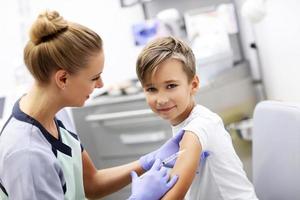 modig liten pojke tar emot injektion eller vaccin med en leende foto