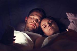ung par använder sig av smartphones i säng på natt foto